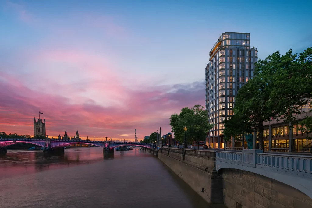 A stunning view of London features the Westminster Tower under a pink and blue sunset. A modern building is pictured to the right, next to a bridge.