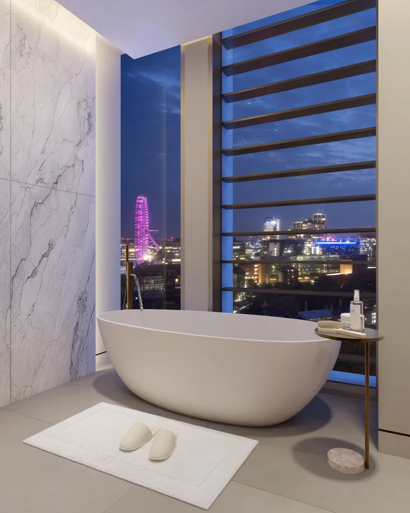 An indoor shot features a modern bathroom with a free-standing tub, slippers on a mat, a marble wall, and a city view at night. The space has a minimalist design and elegant lighting.