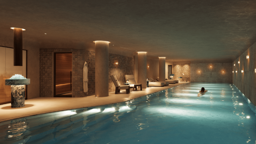 An indoor pool at Trillium Marylebone. The pool is lined with lounge chairs and columns, with a person swimming laps in the water.